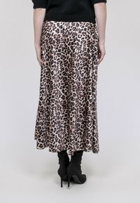 Jupe midi imprimé léopard avec un design fluide, une texture soyeuse et une fente haute, assortie à des bottes à talons noires. Vue arrière présentée.