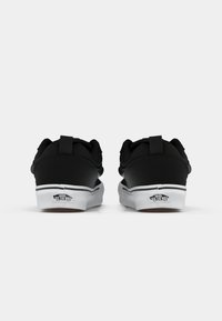 Svarte kanvas sneakers med teksturert overflate, hvit gummisåle og merkevare på hælen. Har kontrasterende svarte stropper og sømmer.