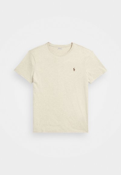 T-shirt de algodão bege com gola redonda e mangas curtas. Apresenta um pequeno logotipo castanho no lado esquerdo do peito. Textura suave, design casual.