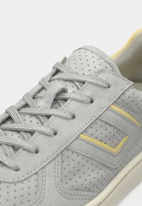 Αθλητικό παπούτσι από γκρίζο σουέντ με διάτρητες λεπτομέρειες, γκρι κορδόνια, κίτρινη ρίγα ως διακοσμητικό και υφασμένο λαστιχένιο πέλμα.