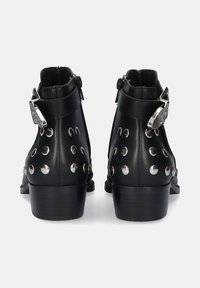Botas de cuero negras hasta el tobillo con tachuelas plateadas, cremalleras laterales y acentos metálicos decorativos, con un tacón bajo y una textura suave.