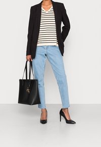 Schwarzer Blazer, gestreifter V-Ausschnitt-Pullover, hellblaue Jeans, schwarze High Heels und eine schwarze Tragetasche mit dekorativem Beschlag.