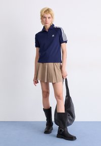 Polo bleu marine à manches courtes avec des rayures blanches, jupe plissée beige et bottes noires jusqu'aux genoux. Sac gris avec une fermeture éclair. Design simple et sportif.