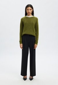 Zelena pletena majica z belim ovratnikom, kombinirana s črnimi širokimi hlačami in koničastimi čevlji. Preprost, teksturiran dizajn, oprijet kroj.