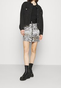 Veste en denim noir sur un haut noir, assortie à une mini-jupe à motifs avec des designs animaliers et floraux, et des bottes noires à lacets.