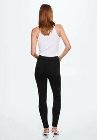 Černé vysoké skinny džíny vyrobené z džínsoviny, s přiléhavým střihem a standardními zadními kapsami. Nosené s bílým topem na ramínka a podpatky.