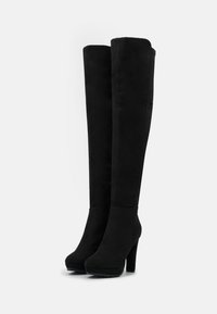 Stivali neri sopra il ginocchio con una texture liscia simile alla suede, alte punte a stiletto e punte arrotondate. Design senza soluzione di continuità con accentuazioni minime.