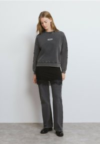 Sudadera gris con logo, cuello redondo y mangas texturizadas. Combinada con una falda negra con encaje y pantalones acampanados grises. Calzado negro.