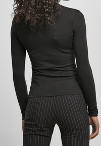 Svart långärmad tröja i ett stretchigt material med en åtsittande design. Kombination med byxor med svarta ränder. Slät yta, inga synliga detaljer.