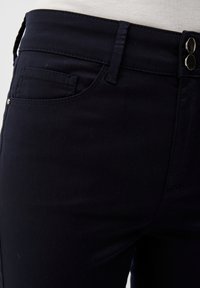 Jean bleu marine en tissu mélangé de coton, avec une poche avant, taille mi-haute et deux boutons métalliques à la taille.