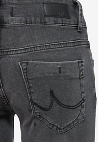 Black denim jeans featuring a slim fit, visible stitching, and a back pocket with a curved design. Matte leather logo patch at the waistband.