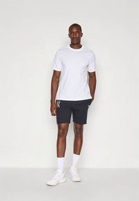 Valge lühikeste varrukatega T-särk tumedate lühikeste pükstega, millel on hele logo. Kandmisel valged pahkluu sokid ja valged tossud.