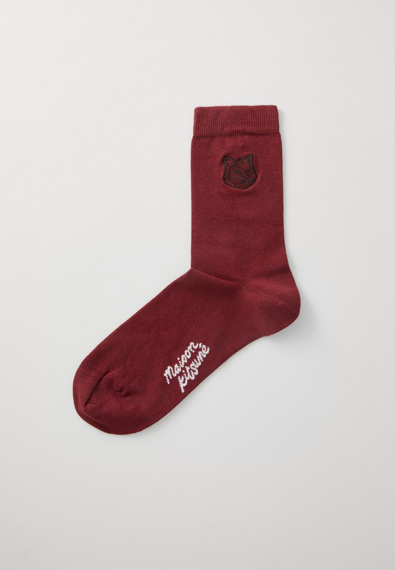 Burgundijas potīšu zeķes no mīksta materiāla ar melnu izšuvumu lapsas seju augšpusē un baltu zīmola uzrakstu blakus pirkstiem.