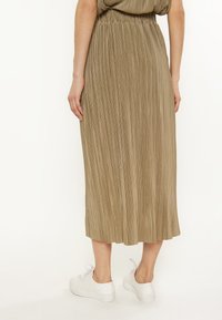 Plisovaná midi sukňa v khaki farbe, s elastickým pásom a voľným siluetou, v kombinácii s bielymi teniskami.