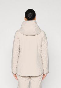 Jachetă izolată bej deschis, cu glugă, cusături vizibile și manșete elastice. Vedere din spate arată un material neted și texturat.