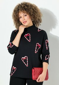 Top nero a maniche lunghe con collo alla coreana, caratterizzato da motivi a cuore a righe rosse e bianche. Tessuto dalla texture liscia. Abbinato a una pochette trapuntata rossa.