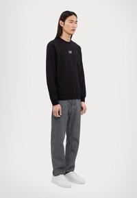 Svart sweatskjorte med ribbestrikkede mansjetter og hem, med et lite logo. Kombinert med grå rette jeans og hvite sneakers. Minimalistisk design.