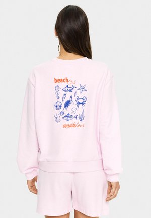 Felpa rosa chiaro con grafiche a tema spiaggia blu, tra cui un cavalluccio marino, un granchio e una stella marina, con il testo "beach Club" e "seasidelove".