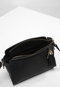 Borsa a tracolla nera in pelle con superficie texturizzata, hardware dorato, chiusura con zip e un accento di nappina staccabile. L'interno presenta diversi scomparti.