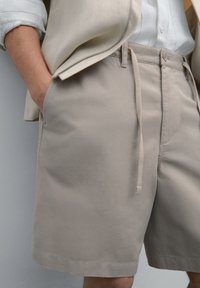 Beige shorts lavet af bomuld, med en snøre i taljen, sidelommer og en glat tekstur. Designet til afslappet brug.