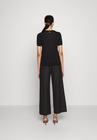 Top nero a maniche corte con una silhouette aderente, realizzato in materiale leggero, abbinato a pantaloni neri a gamba larga e sandali con tacco alto.
