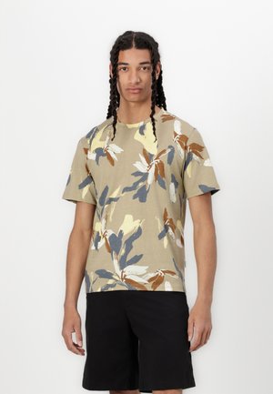 Kortermet, beige t-skjorte med et fargerikt blomsterdesign i nyanser av brunt, blått og gult; kombinert med svarte shorts.