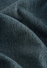 Džínovina s hlbokou modrou farbou, ktorá má textúrovaný povrch a diagonálny vzor tkaniny, zobrazujúci mäkké záhyby a vrásky.