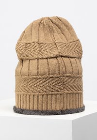 Bonnet tricoté en marron clair avec des motifs côtelés et en tissage de panier, présentant une doublure en fausse fourrure grise au bord inférieur.