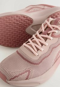 Scarpe da ginnastica rosa chiaro con tomaia in rete testurizzata, dettagli lisci e suola in gomma con un design curvo e motivo.