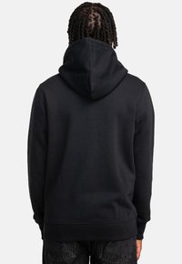 Schwarzer Hoodie mit großer Kapuze, gerippten Bündchen und einem strukturierten Fleece-Material, von hinten gezeigt.