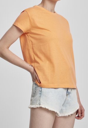 Pomarańczowa bawełniana koszulka z krótkim rękawem, okrągłym dekoltem i luźnym krojem, w zestawie z jasnoniebieskimi dżinsowymi szortami z postrzępionymi brzegami.