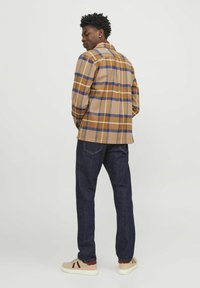 Bruine en blauwe geruite jas met een kraag, lange mouwen, gecombineerd met donkere spijkerbroek en beige sneakers. De stof lijkt textuur te hebben.
