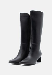 Bottes noires en cuir montantes avec un bout pointu et un talon bloc. Fermeture éclair sur le côté et texture lisse, présentant des détails de conception minimaux.