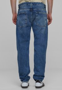 Lysblå denimbukser med lige ben, to baglommer og synlige stikninger. Matchet med sorte og hvide sko.
