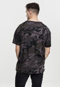 Kortermet t-skjorte i mørkt camouflage-mønster, med løs passform, rund hals og myk bomullsstoff.