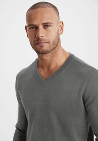 Grauer V-Ausschnitt-Pullover aus weichem Material, mit langen Ärmeln und glatter Textur, geeignet für legere oder smart-legere Anlässe.