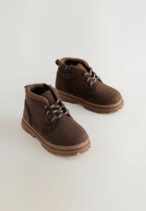 Bruna ankelboots med en mjuk textur, med snörning fram och en siddragkedja, placerade på en slitstark gummisula för bra grepp.