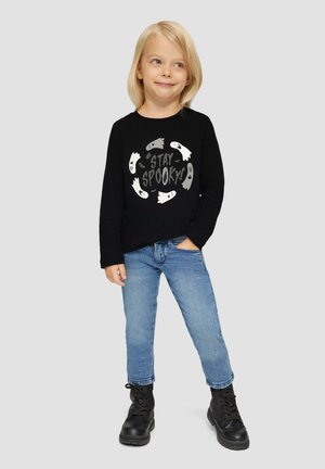 Zwarte lange mouwen shirt met de tekst "Stay Spooky" en grafische afbeeldingen van geesten, gecombineerd met blauwe jeans en zwarte laarzen. Kind staat zelfverzekerd.