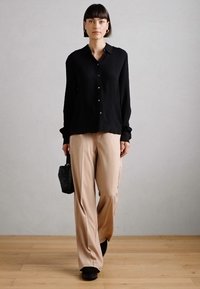 Camisa preta de botões com colarinho, combinada com calças largas bege. Tecido texturizado, usada com uma pequena bolsa preta e sapatos escuros.
