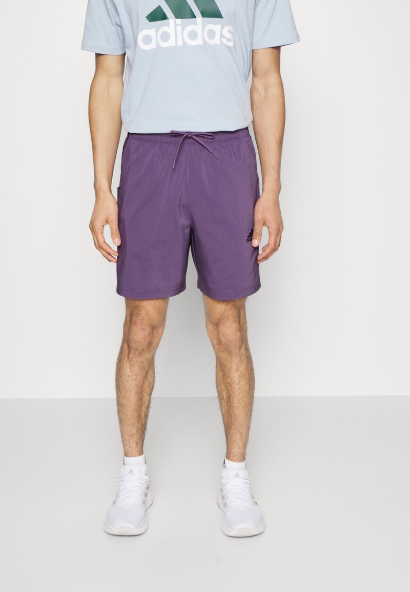 Fialové sportovní šortky s elastickým pasem a stahovací šňůrkou. Černé logo Adidas na boku. Nosené s světle modrým tričkem Adidas a bílými teniskami.