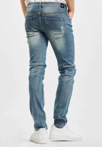 Blå denimjeans med slank passform, falmet finish, lappering på baklommene og subtil slitasje. Kombinert med hvite sneakers.