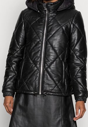 Zwarte doorgestikte capuchonjas met rits aan de voorkant, elastische boorden en trekkoord in de zoom, gedragen over een zwarte leren rok.