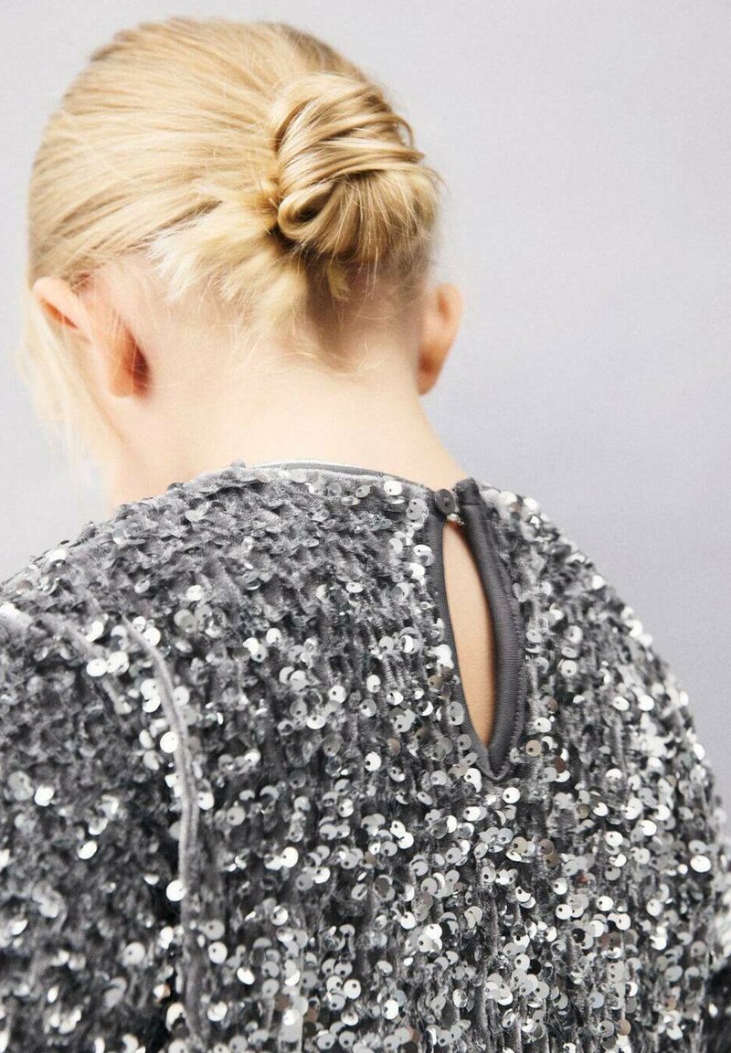 Haut gris à sequins avec une surface texturée, doté d'une fermeture à boutons et d'un détail de dos en forme de trou clé. Tissu lisse avec des embellissements brillants.
