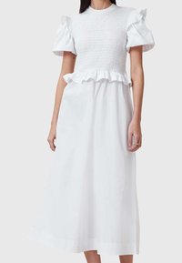 Vestido blanco hecho de una tela ligera. Presenta un corsé fruncido, mangas con volantes y una falda acampanada que llega hasta la mitad de la pantorrilla.