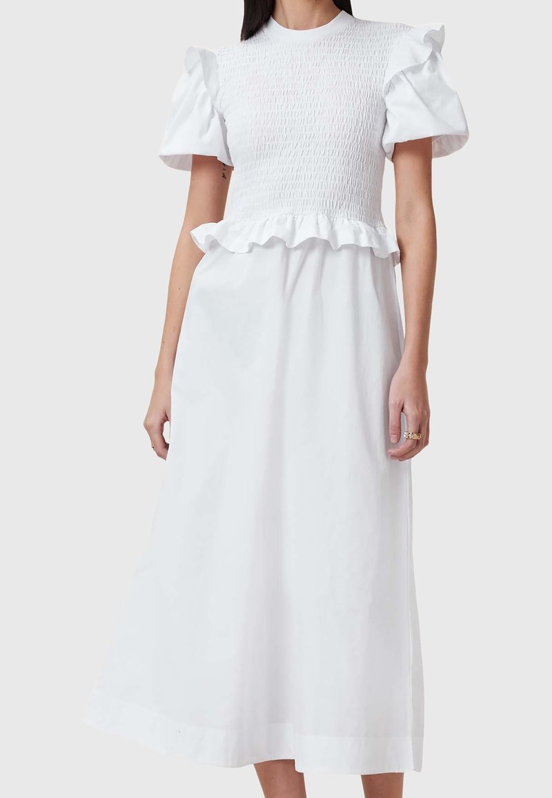 Vestido blanco hecho de una tela ligera. Presenta un corsé fruncido, mangas con volantes y una falda acampanada que llega hasta la mitad de la pantorrilla.