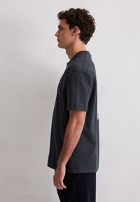 Ciemnoszary t-shirt z krótkim rękawem i okrągłym dekoltem. Charakteryzuje się minimalistycznym wzorem i miękką, bawełnianą fakturą. Bez widocznych logo ani wzorów.