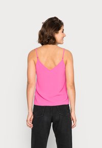 Top fúcsia com alças finas e design às costas em V, feito de um tecido macio. Combinado com calças pretas de cintura alta.