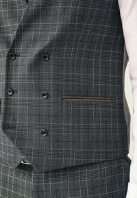 Gråternet vest lavet af tekstureret stof, med seks sorte knapper, en smal brun lomme trim, og et traditionelt dobbeltbrystet design.
