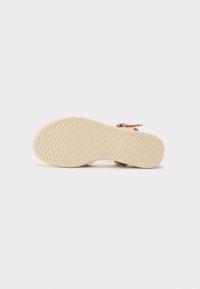 Lys brun sandal såle med et teksturert mønster, som har et lavprofildesign og en metallisk aksent nær ankelstropen.