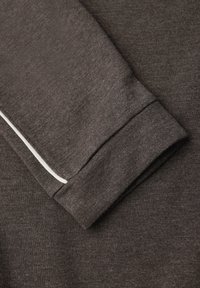 Dunkelbraunes Langarmkleidungsstück mit einem gerippten Bündchen, das eine weiße Akzentlinie entlang der Naht hat. Weiche Textur, figurbetonter Schnitt.